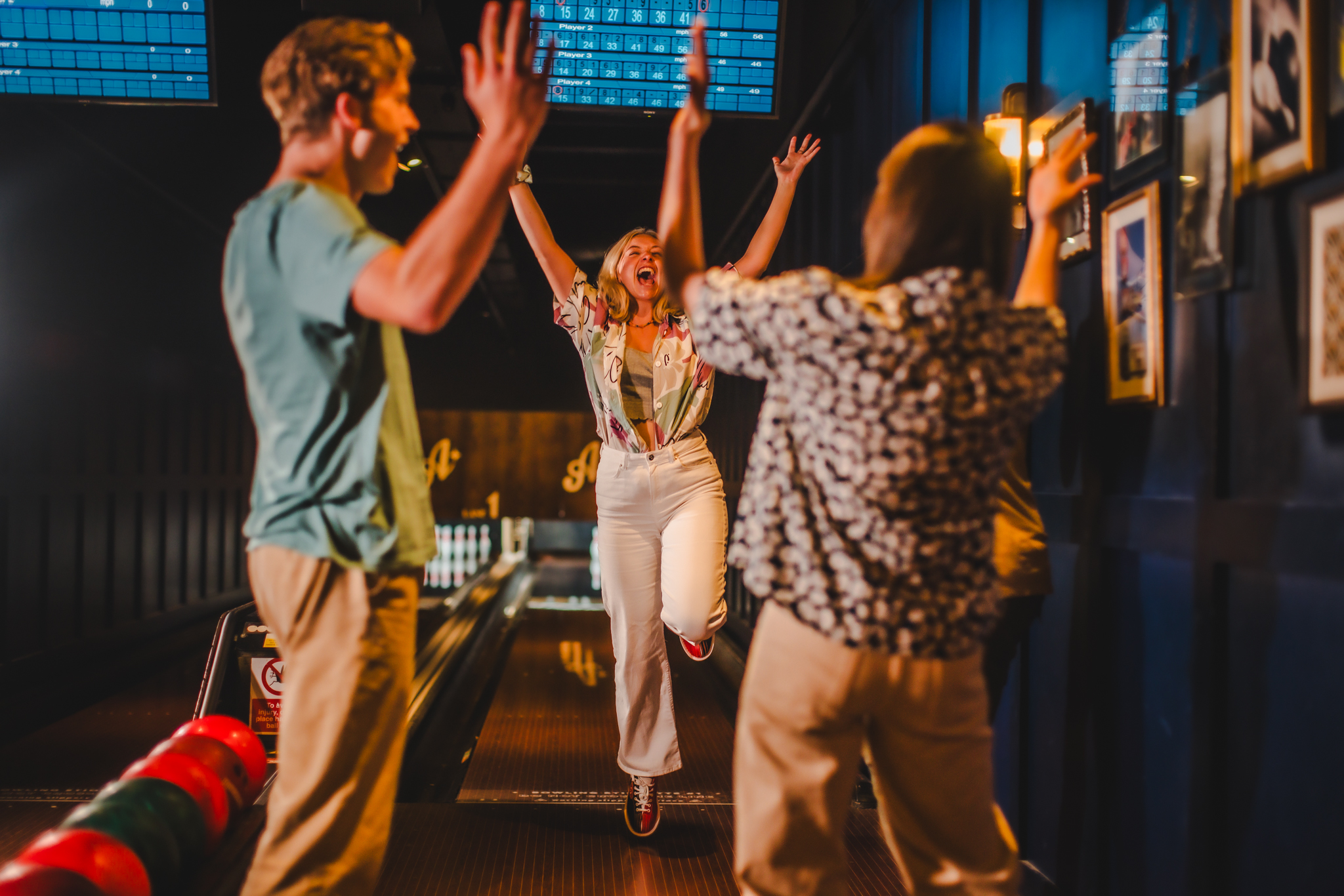 A woman in a bowling alley raising her arms and celebrating.