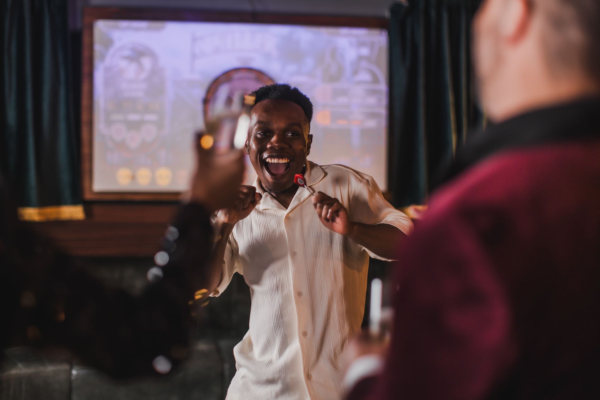 A joyful man enjoying himself at a lively party, surrounded by friends whilst holding a dart in his hand.