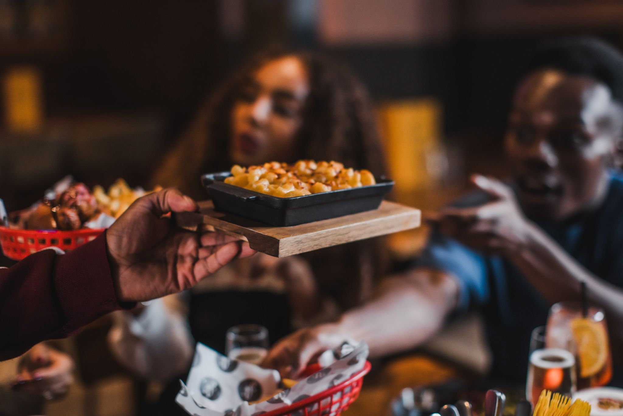 A hand holding macaroni and cheese in front of a male and female.