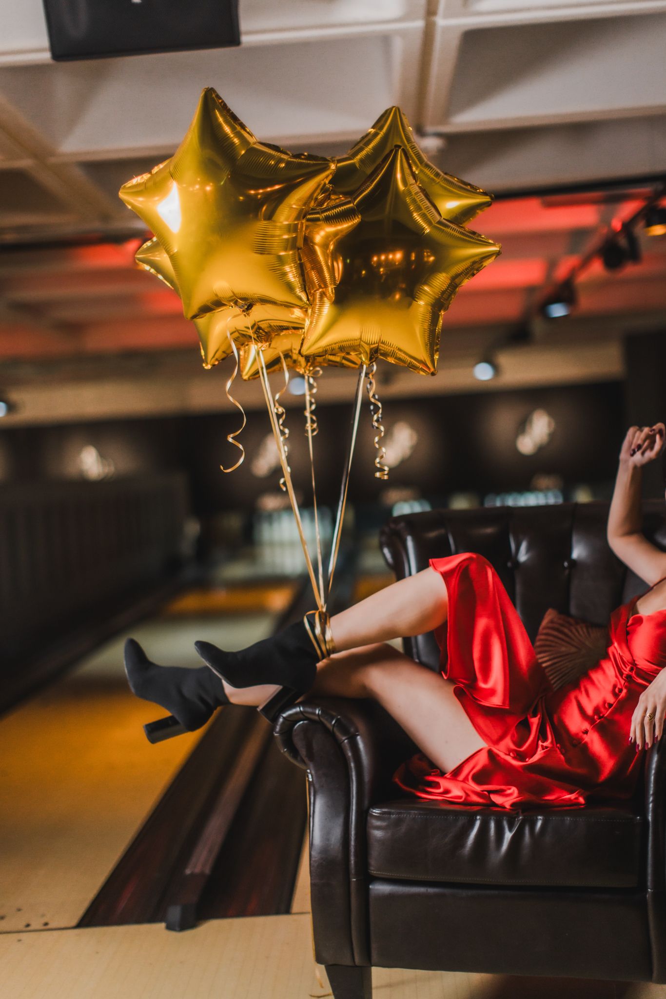 A female sitting in a chair with gold balloons attached to her feet.