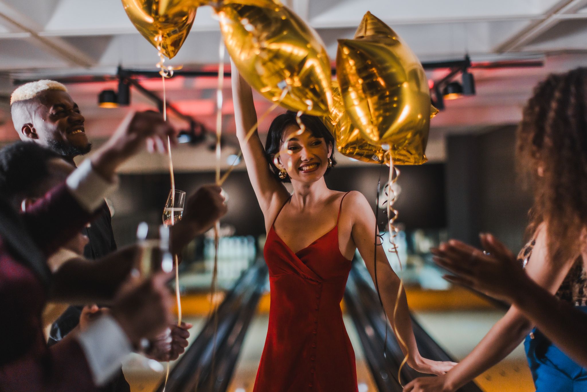 A female in a dress surrounded by balloons in a bowling alley.