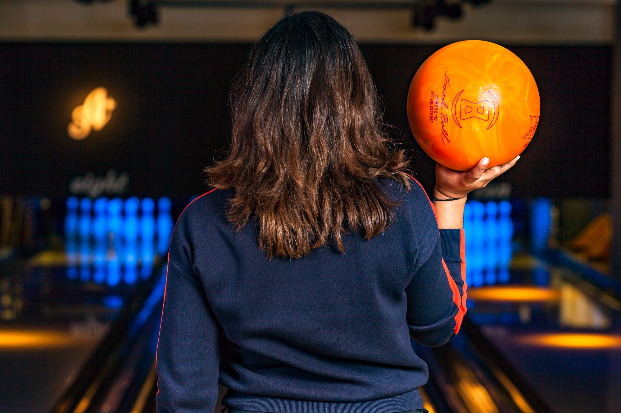 A female holding up a bowling ball whilst showing the back of her head with mid length hair.