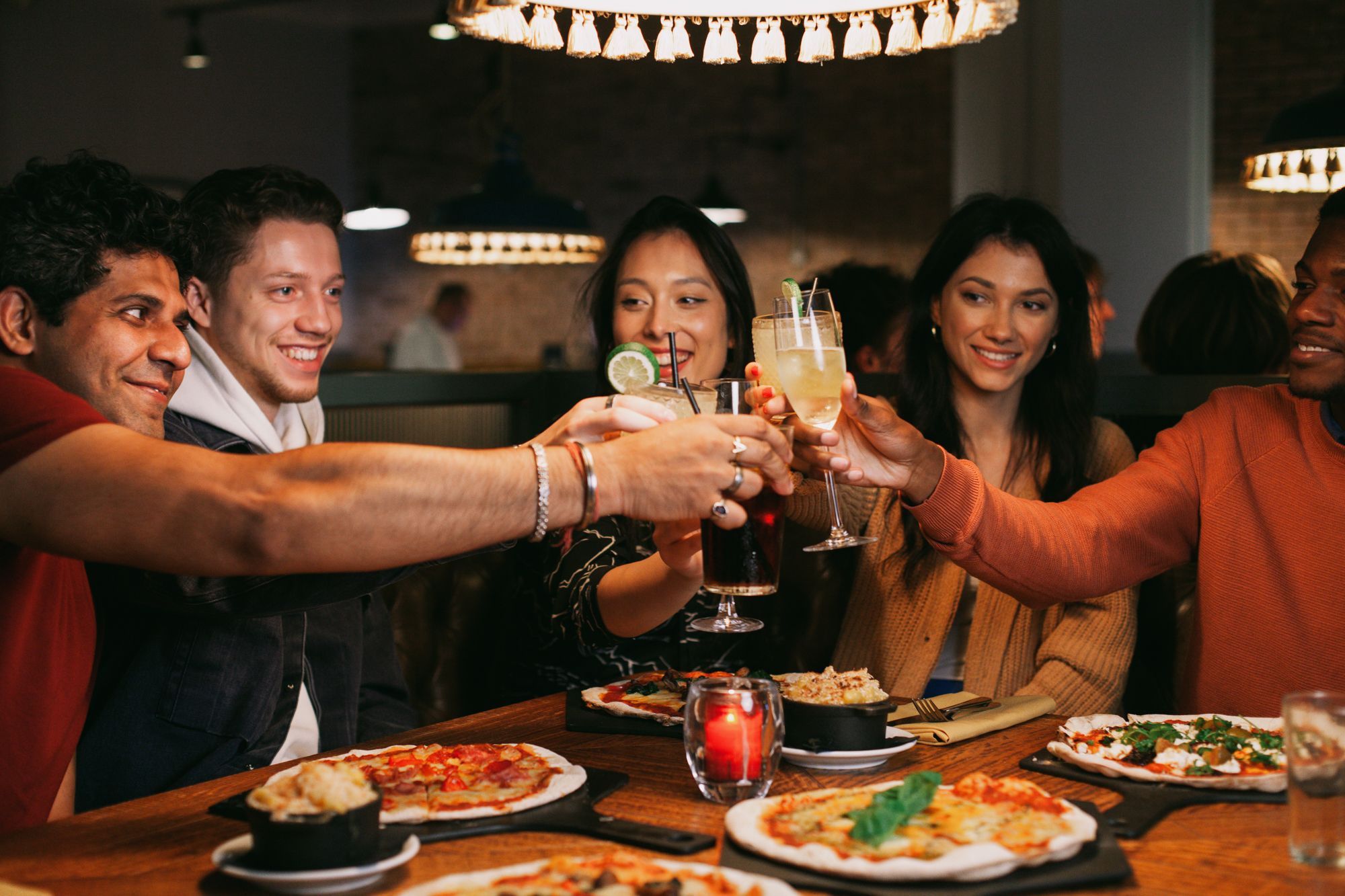 A group of individuals joyfully toasting with drinks at a restaurant, celebrating a special occasion together.