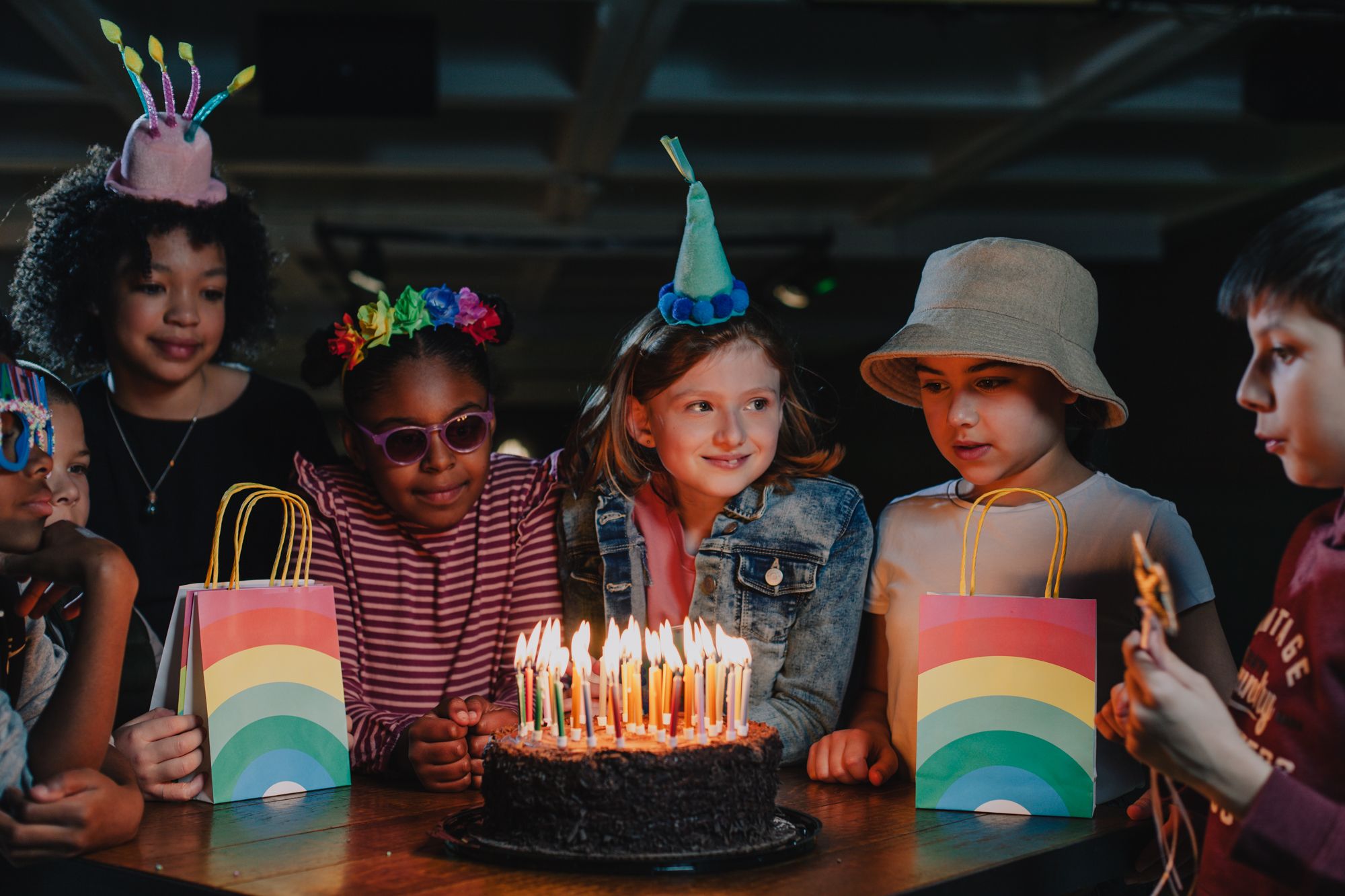 A group of children surrounding a birthday cake with candles on.